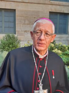 Mgr Luc Ravel en habit d'archevêque avec la croix pectorale, dans la cour de l'Institut